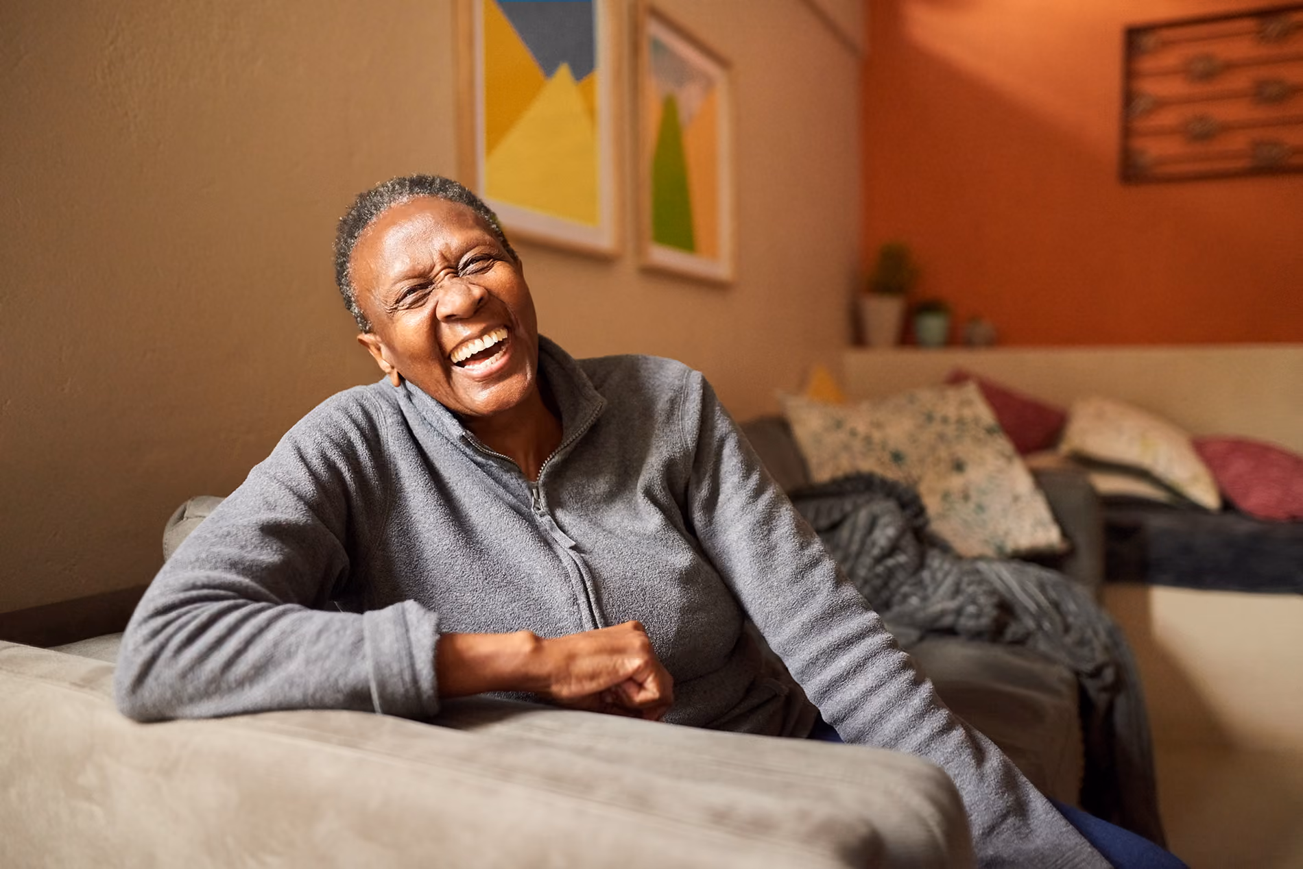 A person is sitting on a couch, smiling and laughing joyfully indoors.