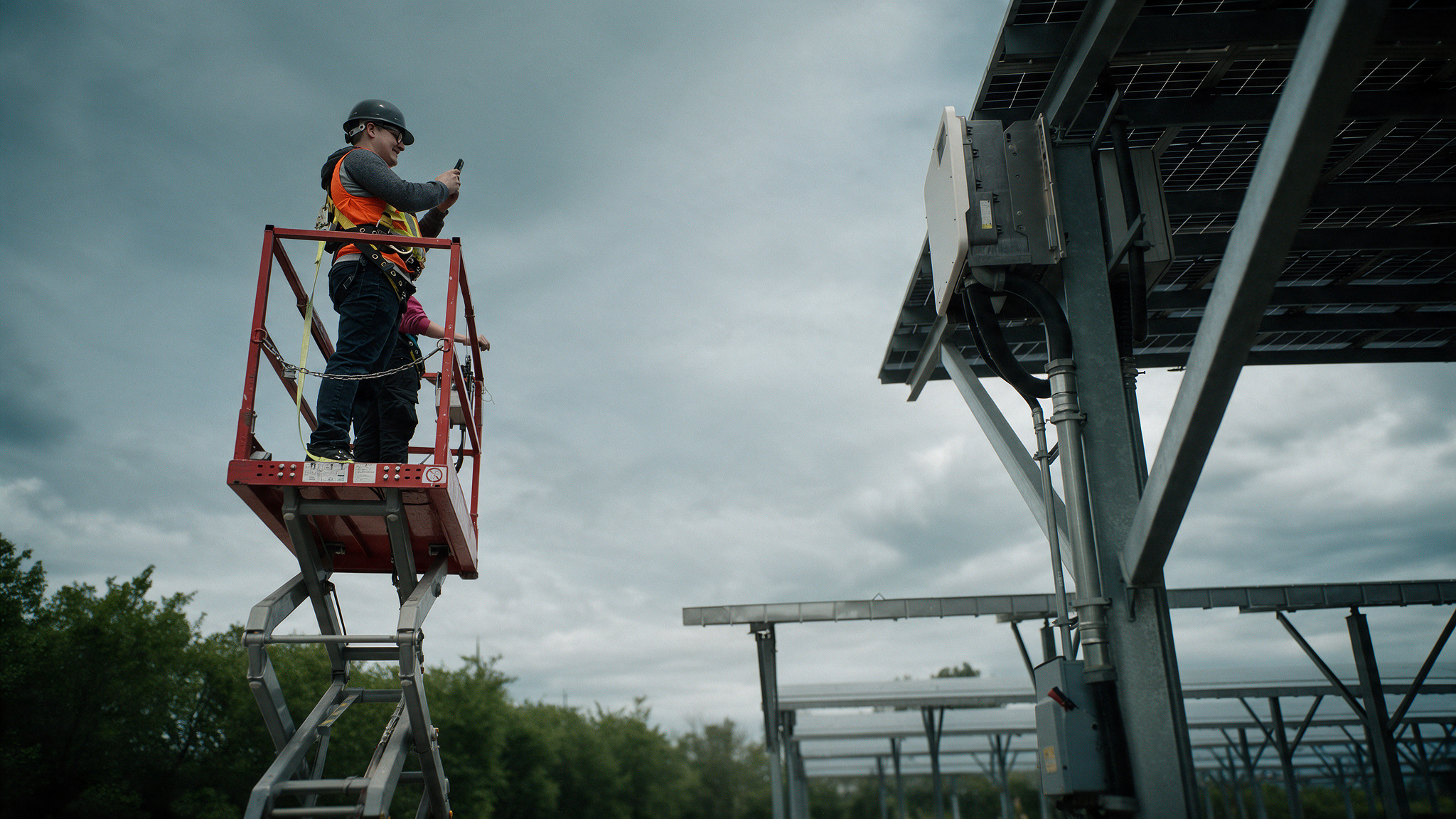 Field inspector on a lift photographing a solar canopy with a mobile phone