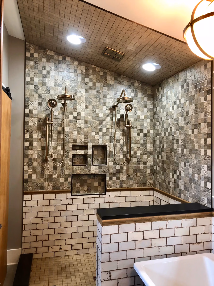 Tiled walk-in shower with dual shower heads, built-in wall niches, and white brick half walls with a dark bench cap