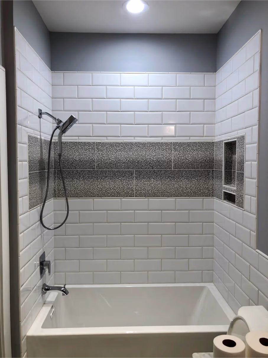 White subway tile tub and shower surround with a gray accent band, built-in niche, and modern chrome fixtures