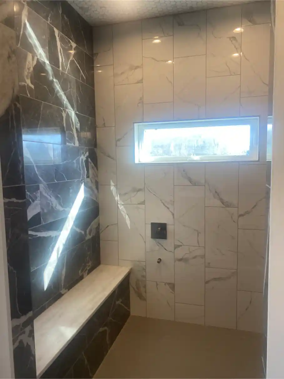 Shower interior with two-tone marble tile, dark marble accent wall with built-in bench, light marble on remaining walls, and a small transom window