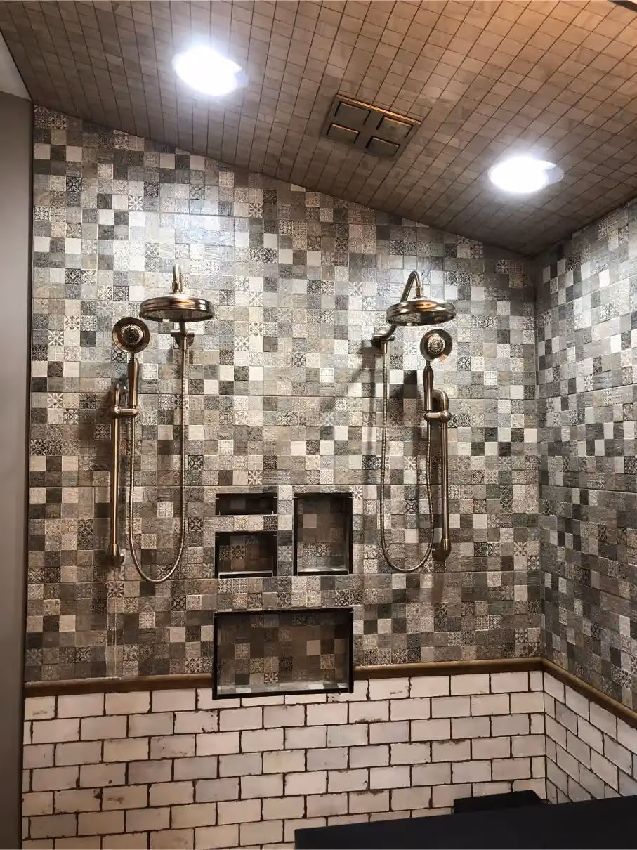 Close-up of a custom shower with patterned gray wall tile, dual shower heads, multiple built-in niches, and white brick half walls