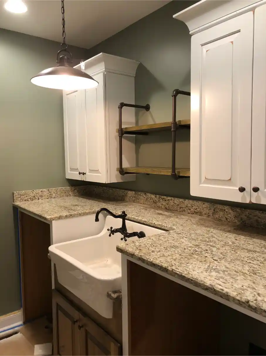 Utility-style vanity area with granite countertops, apron-front sink, white upper cabinets, open pipe shelving, and pendant lighting
