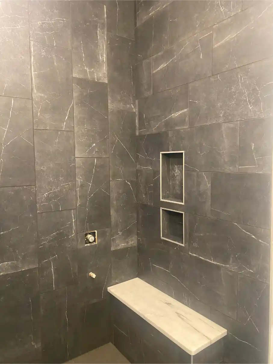 Dark marble-look shower with a floating bench, recessed niches, and large-format wall tile with subtle white veining