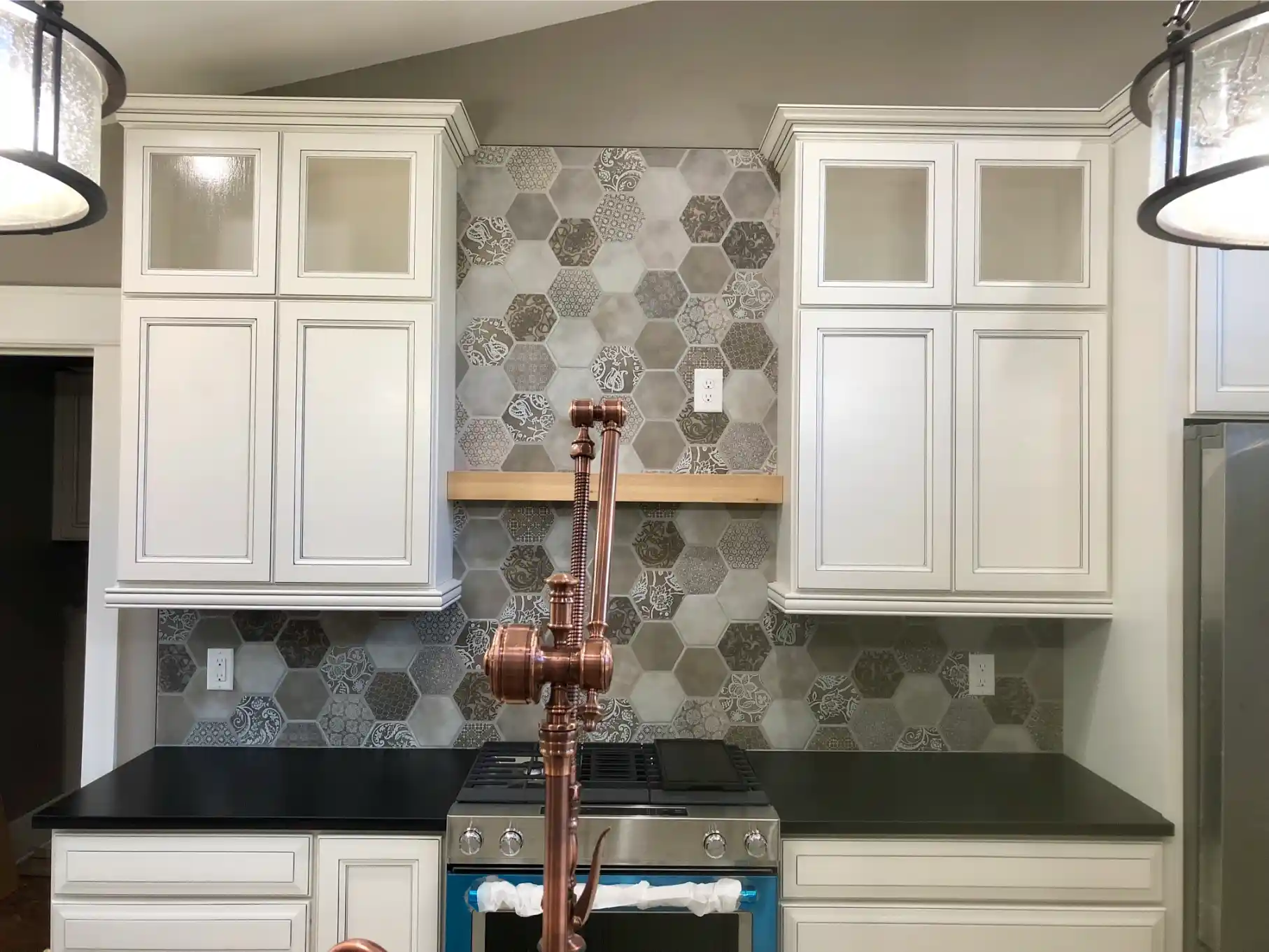 Kitchen range wall with white shaker cabinets, dark countertops, stainless steel stove, and a patterned gray hexagon tile backsplash