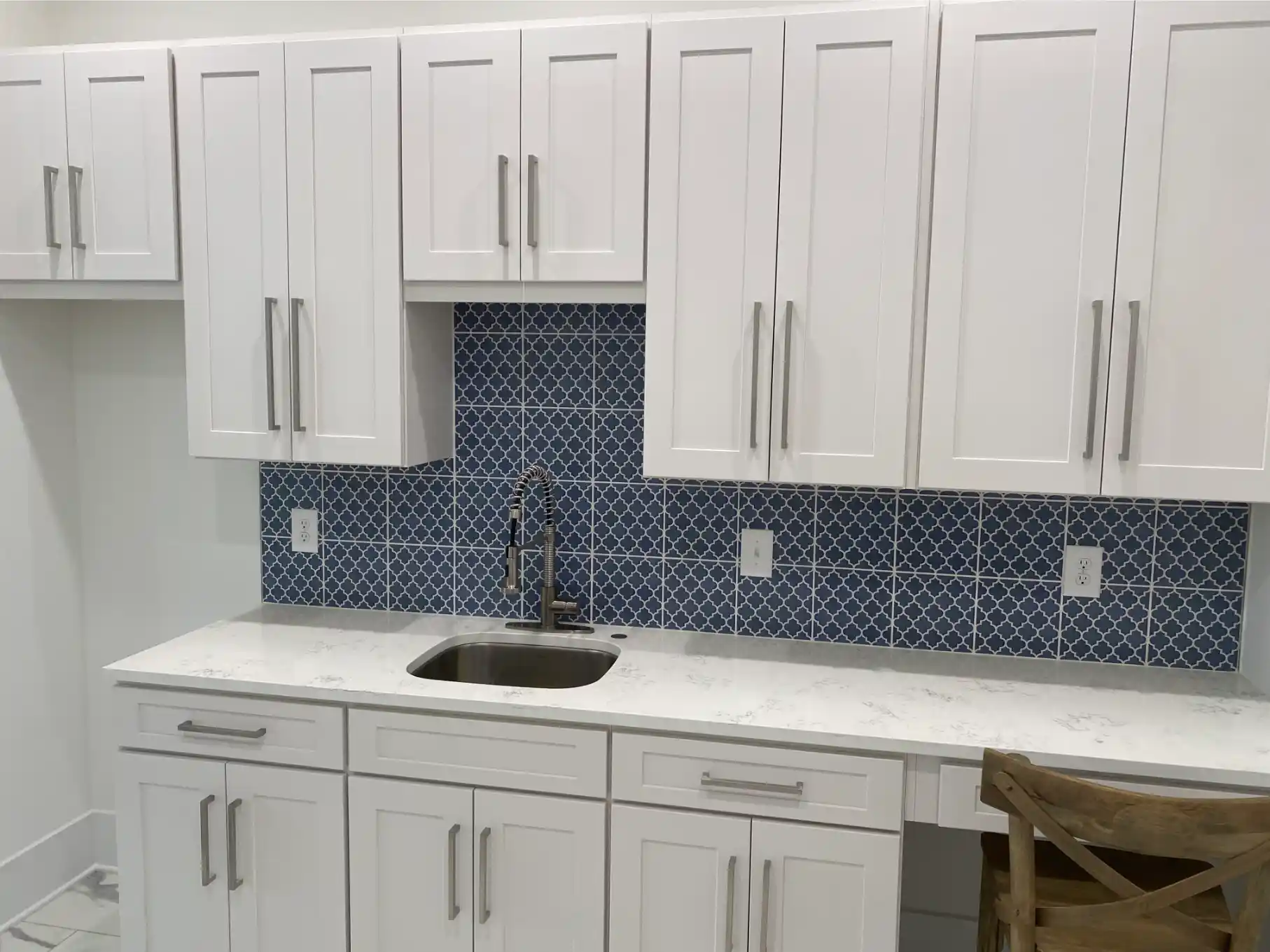 White cabinetry with a blue patterned tile backsplash, undermount sink, quartz countertop, and built-in desk seating area