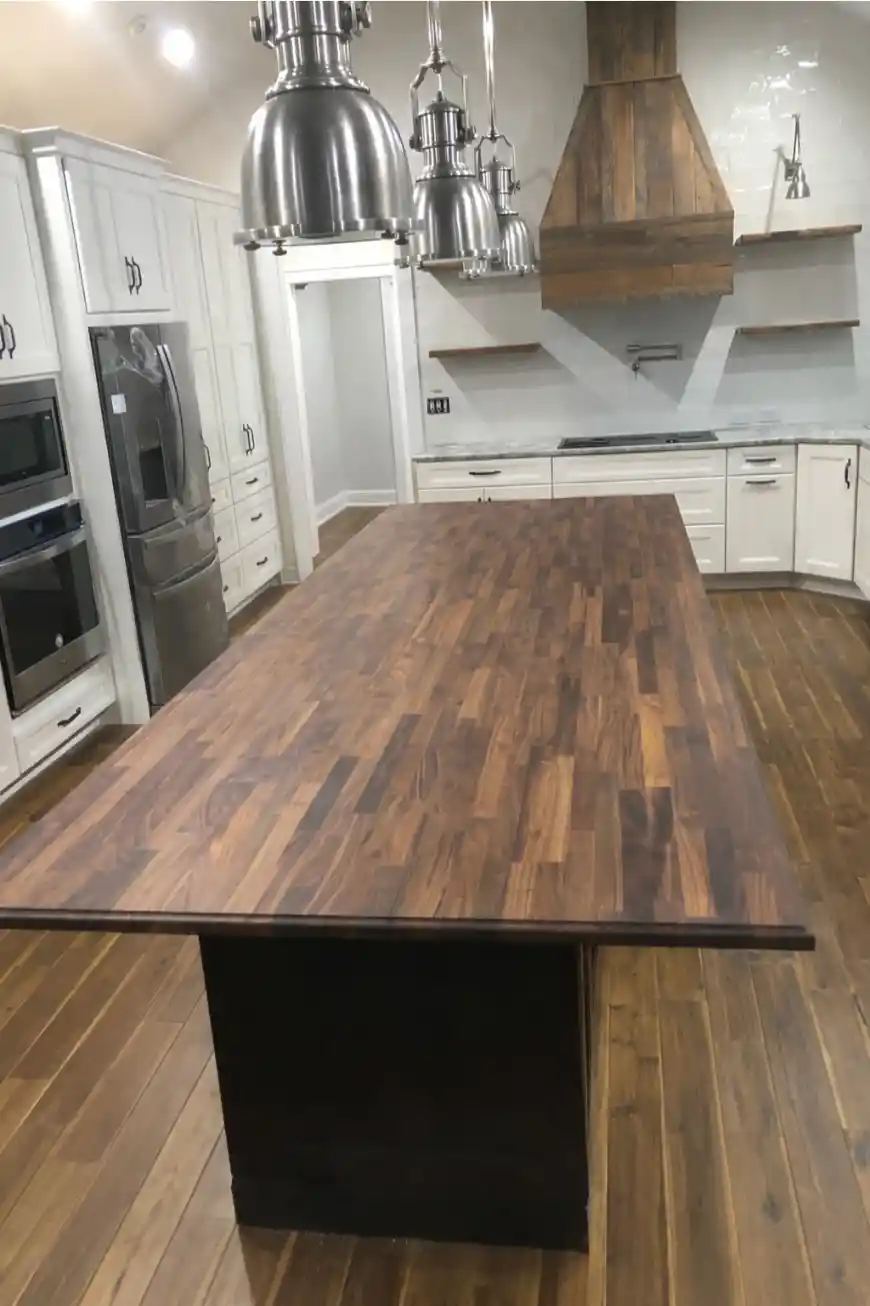 Spacious kitchen with a large walnut island, white cabinets, stainless appliances, industrial pendant lights, and a wood range hood
