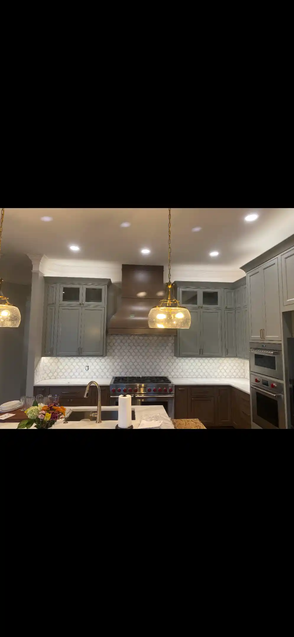 Gray and dark wood kitchen with a central island, decorative tile backsplash, stainless range, and built-in wall ovens
