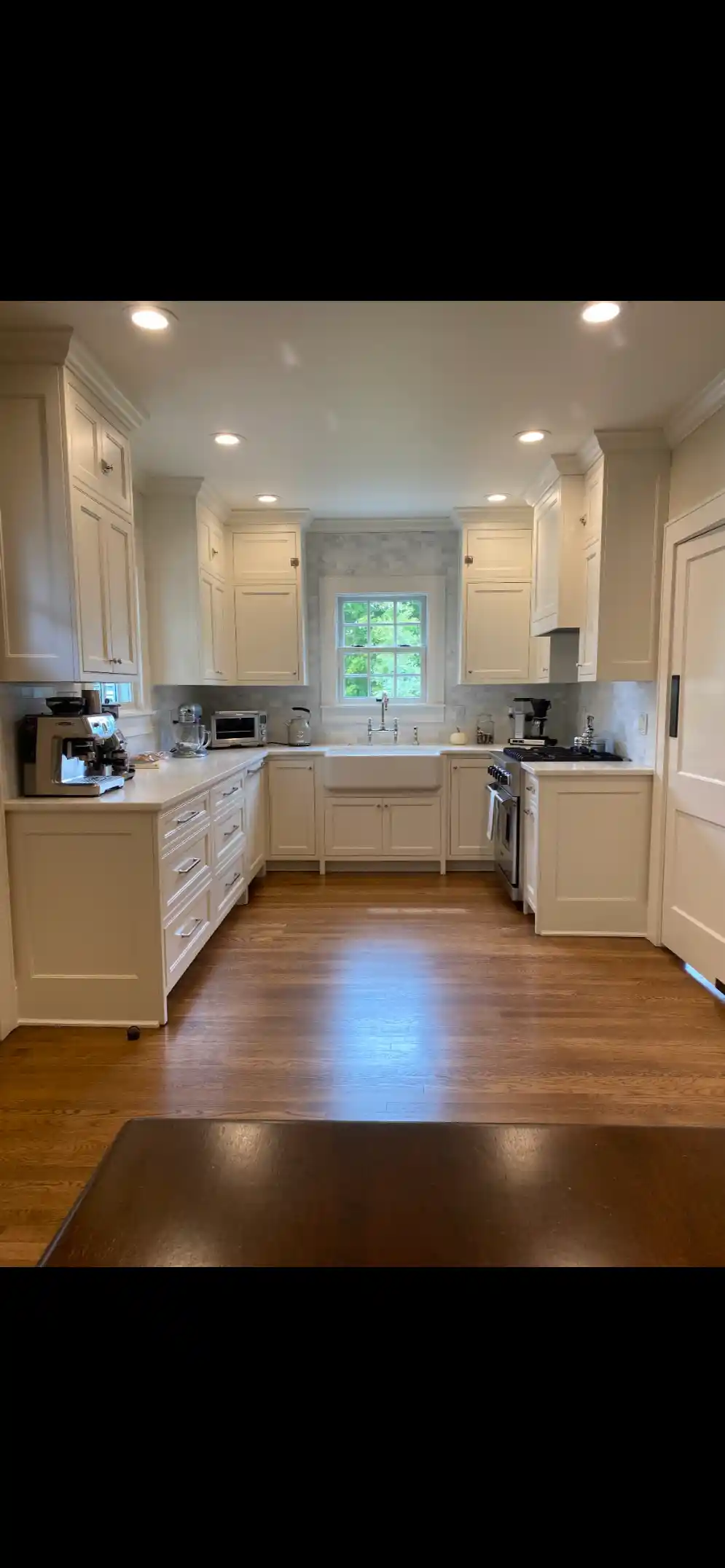 Bright kitchen with cream shaker cabinets, apron-front sink beneath a window, white countertops, and hardwood floors