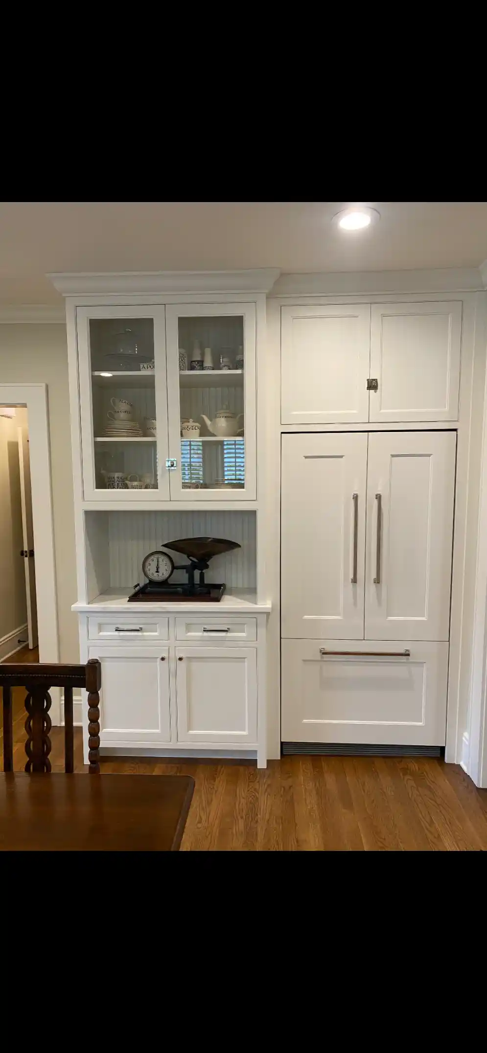 White kitchen hutch and pantry built-ins with glass-front upper cabinet, beadboard backing, and wood flooring