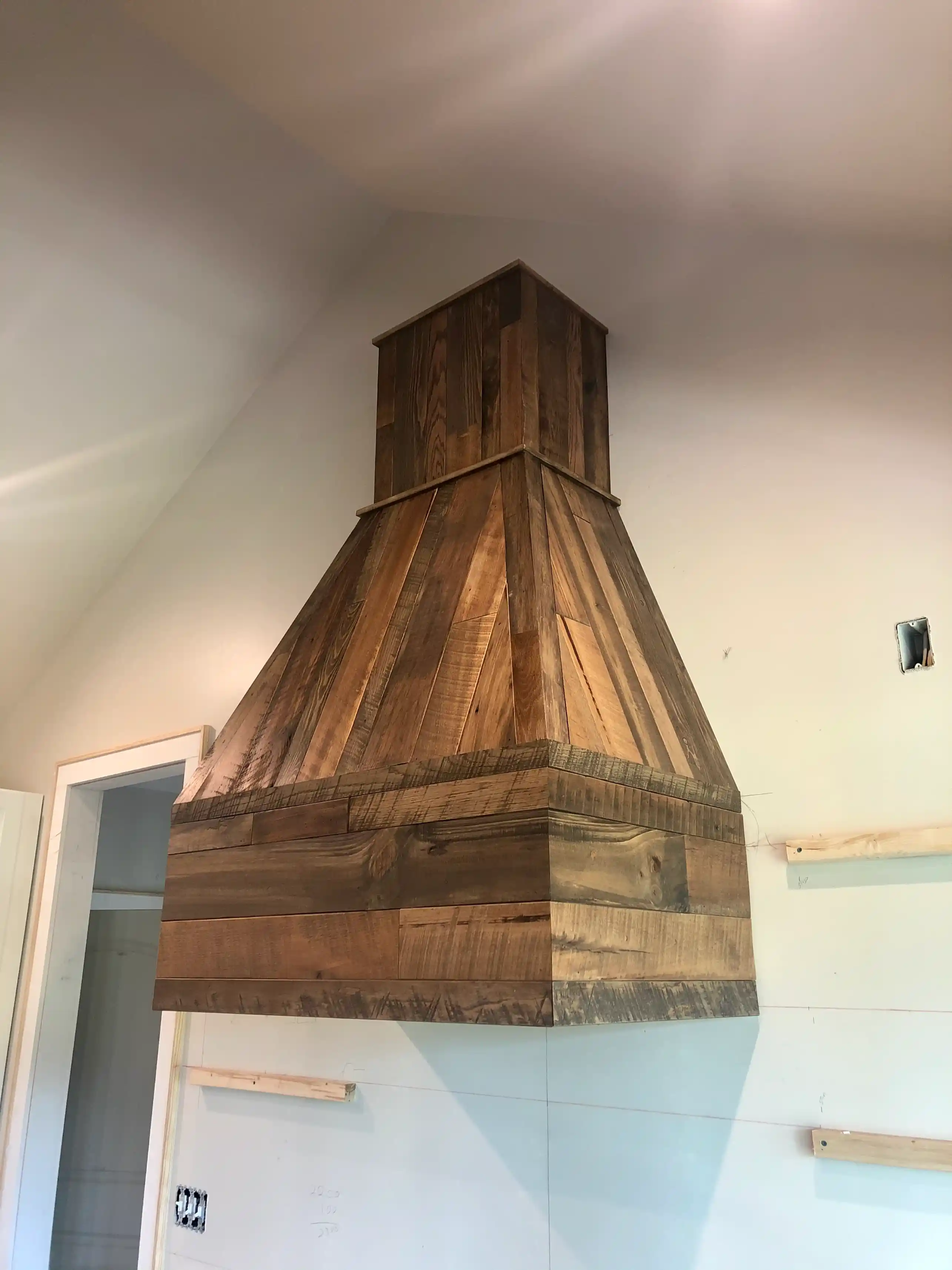 Close-up of a custom reclaimed-wood range hood with tapered chimney design and mixed-toned plank construction