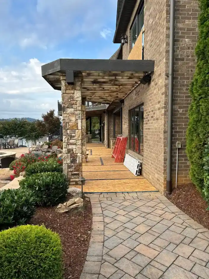 Stone-column covered walkway along a brick home with paver path, landscaped shrubs, and mountain views in the background