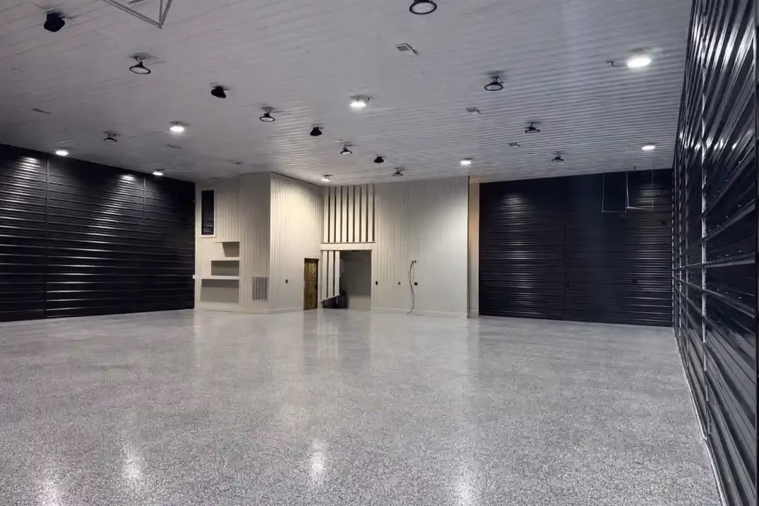 Large finished garage or showroom space with speckled epoxy flooring, black paneled walls, white accent walls, and recessed lighting