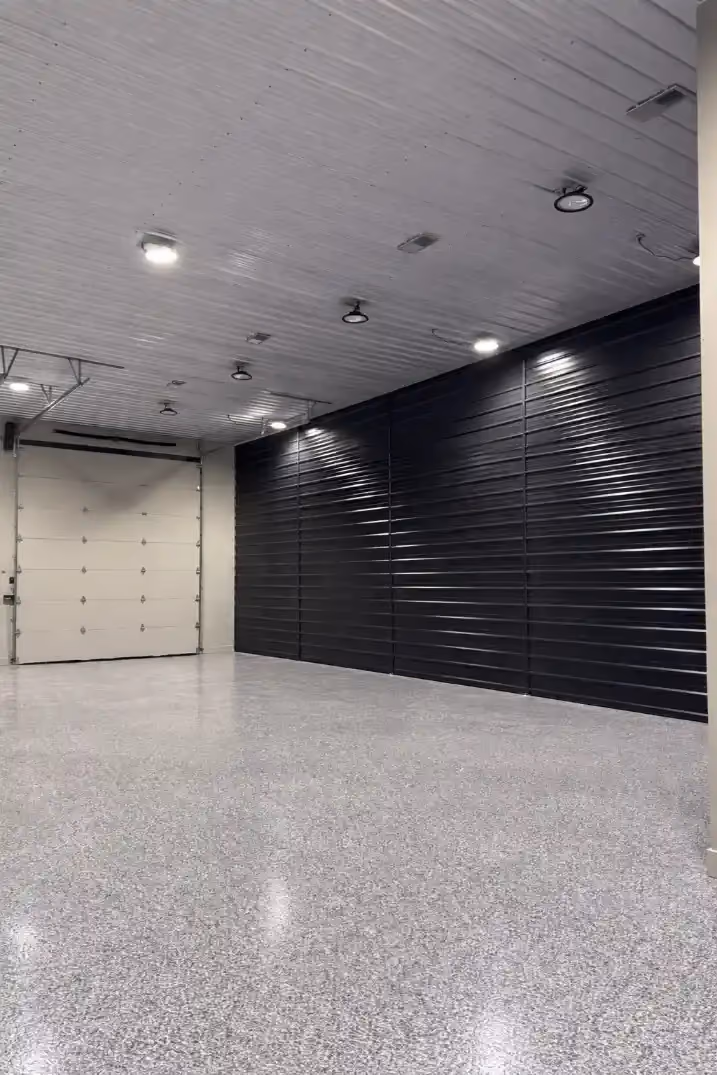 Finished garage interior with speckled epoxy floor, black horizontal wall panels, white garage door, and recessed ceiling lights