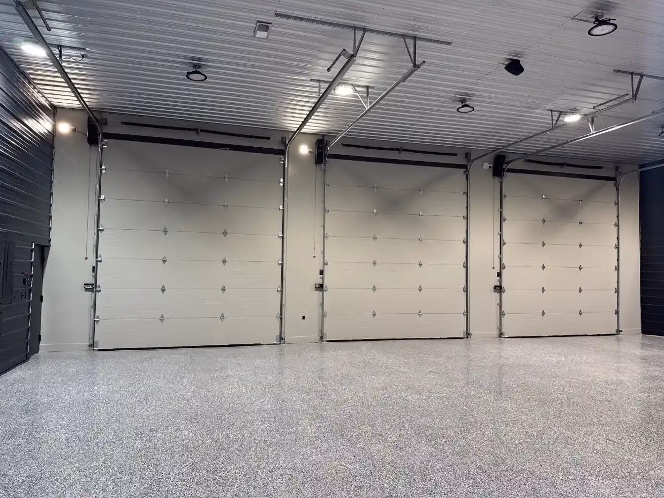 Three-car garage interior with epoxy flooring, paneled overhead doors, and a bright white ceiling with exposed door tracks