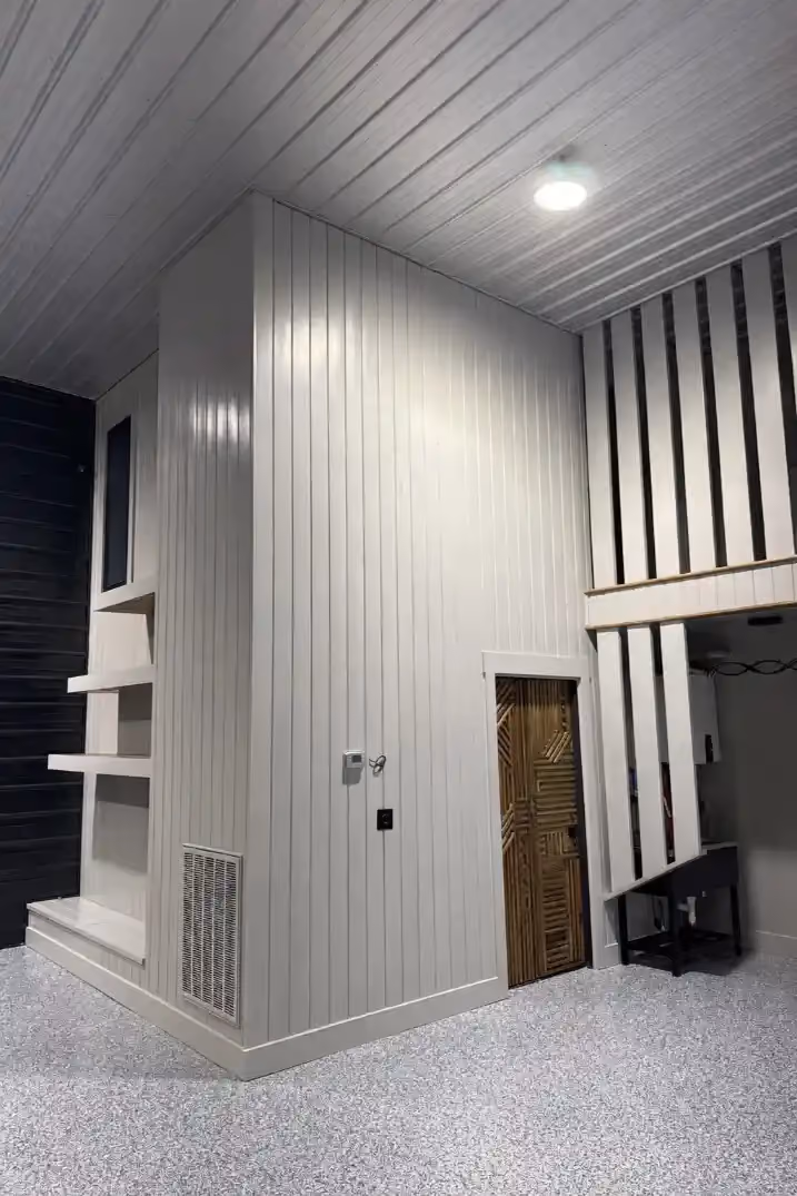 Interior feature wall in a finished garage or flex space with vertical paneling, open display shelves, and decorative trim details