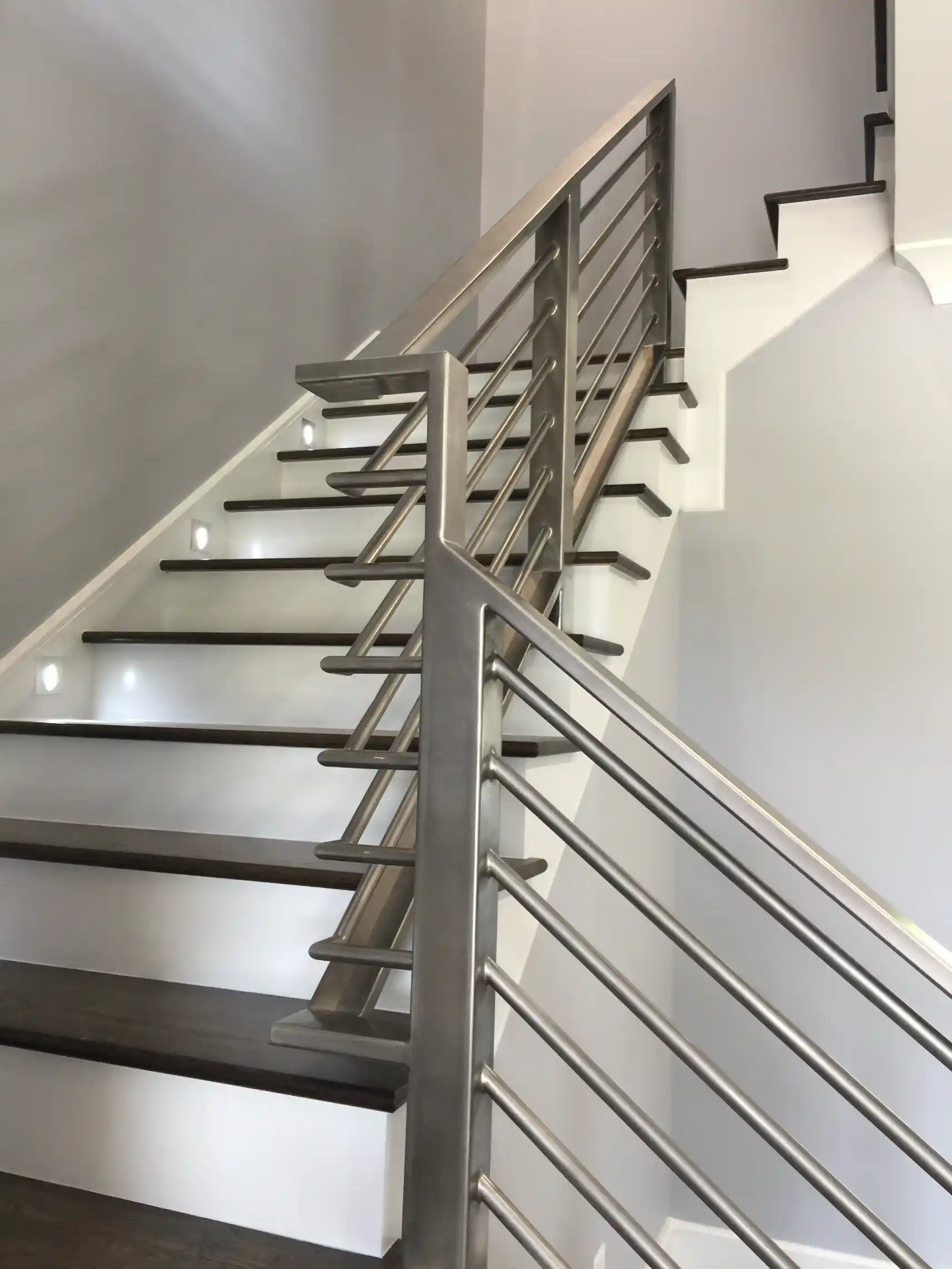 Modern staircase with dark wood treads, white risers, integrated step lights, and brushed metal horizontal railings