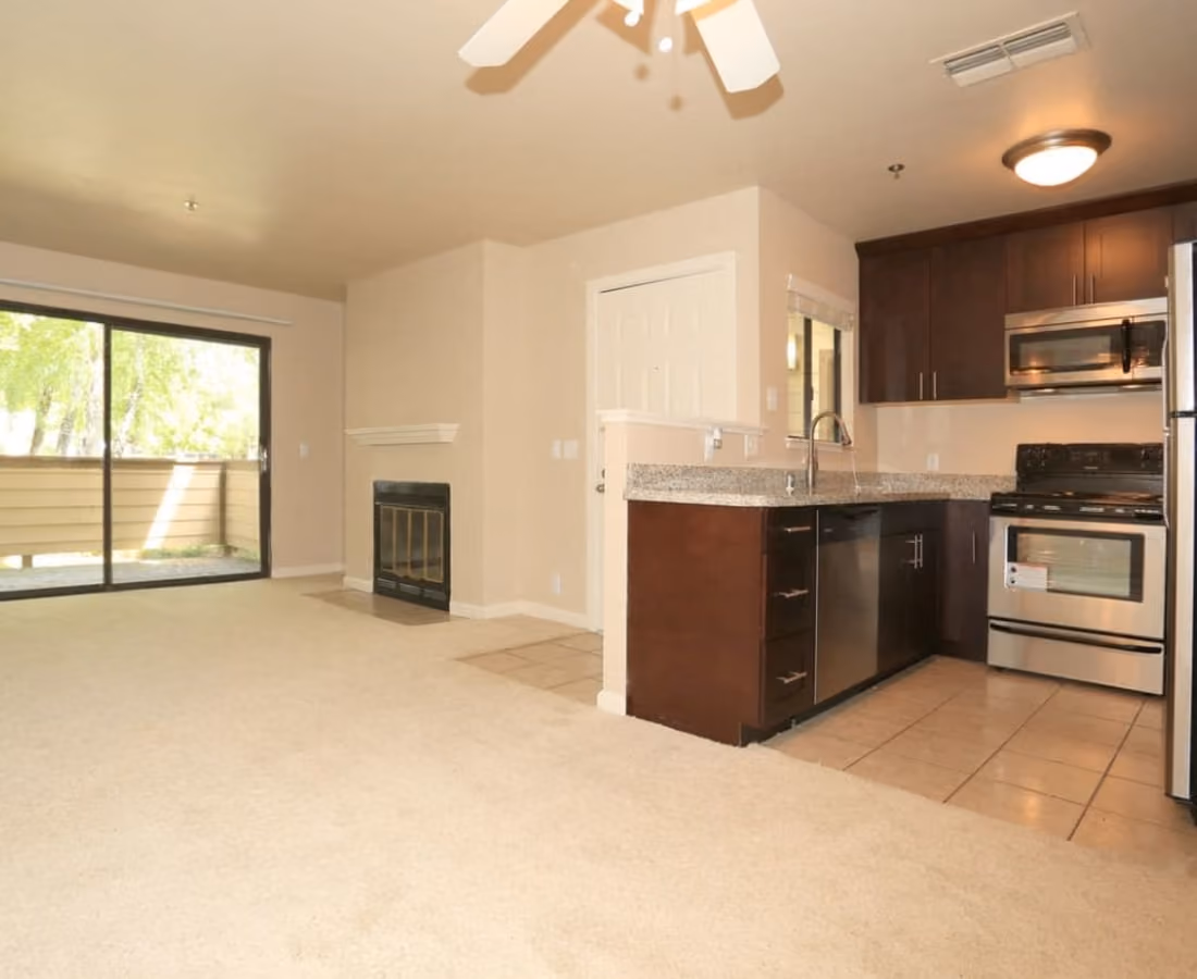 Unfurnished living area with fireplace, patio sliding doors, and Kitchen with brown cabinets and stainless steel appliances