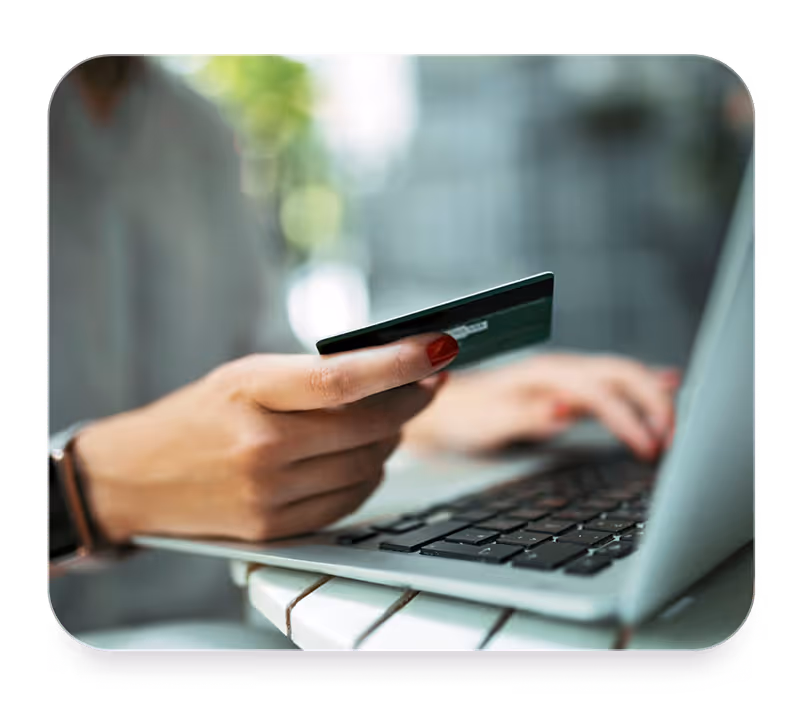 Person holding a credit card while using a laptop keyboard for online payment.