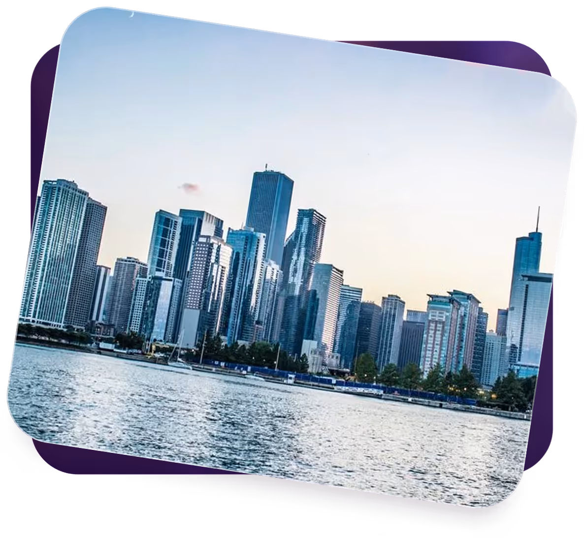 City skyline of tall modern skyscrapers along a waterfront under a clear sky at dusk.
