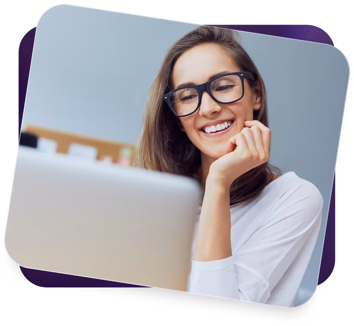 Smiling woman wearing glasses working on a laptop with hand resting on her chin.