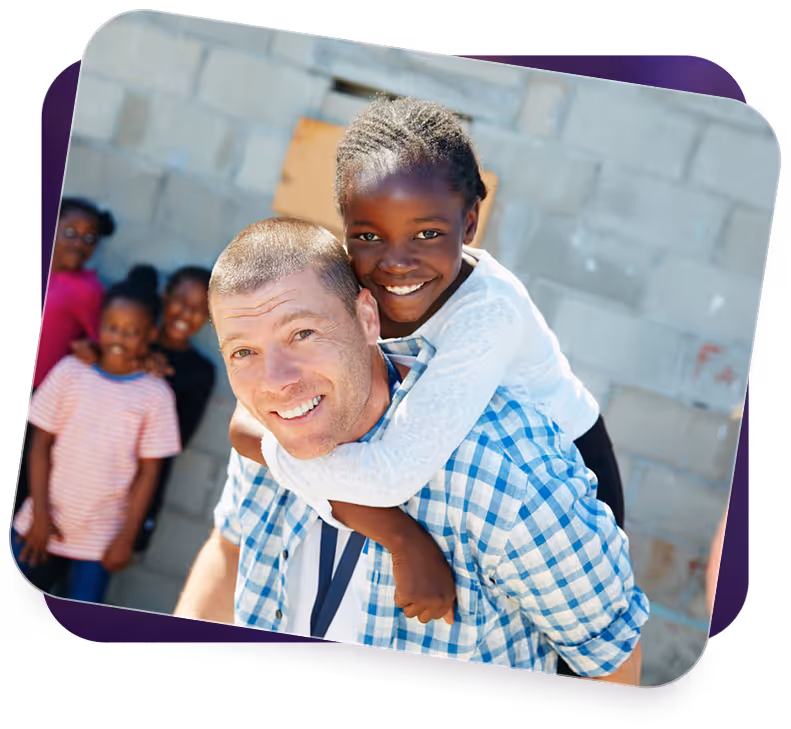 Smiling man giving piggyback ride to happy girl with other children in background.