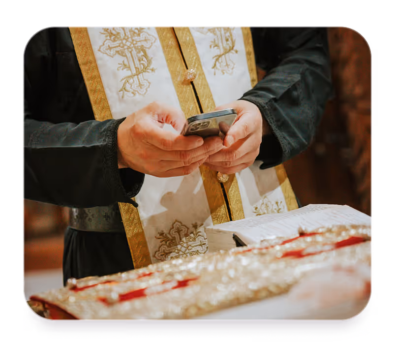 Priest in ornate vestment holding a smartphone over an open religious book on altar.