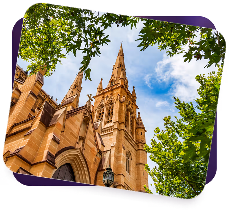 Gothic-style church towers with pointed spires framed by green tree branches and a partly cloudy sky.