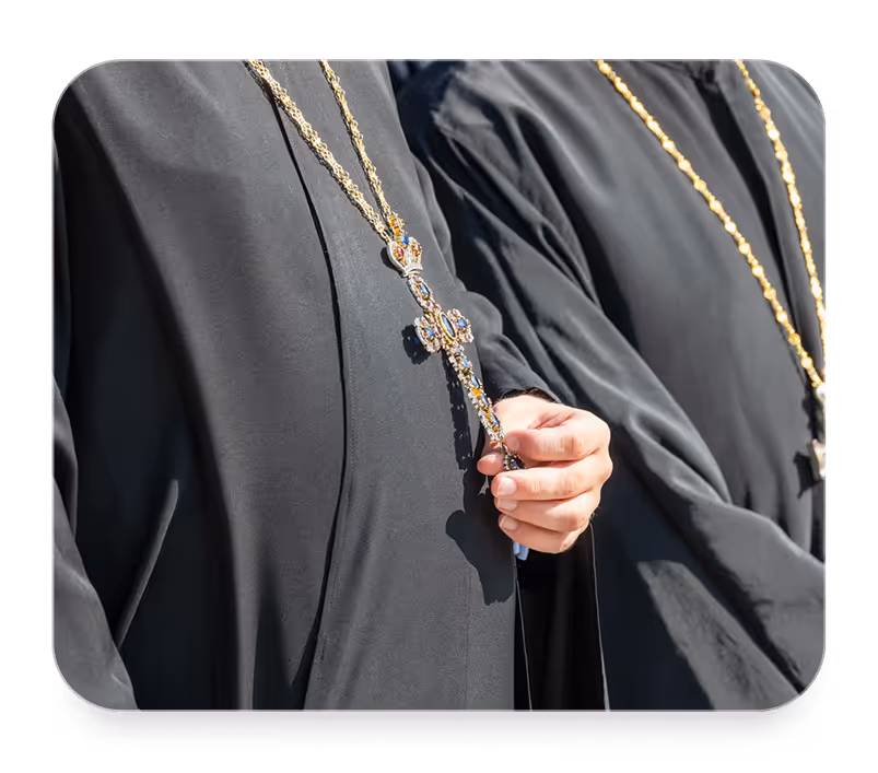 Two clergy in black robes wearing gold chains with ornate crosses, one holding a jeweled cross.