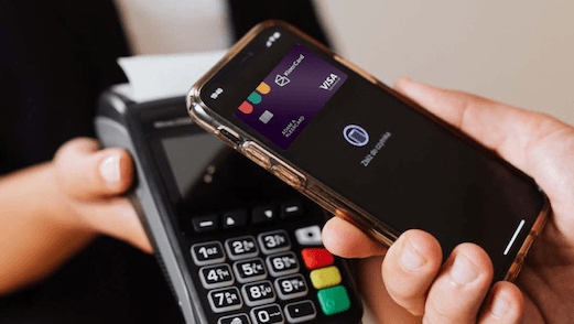 Hand holding smartphone with digital Visa card near a card payment terminal for contactless payment with KleerCard.