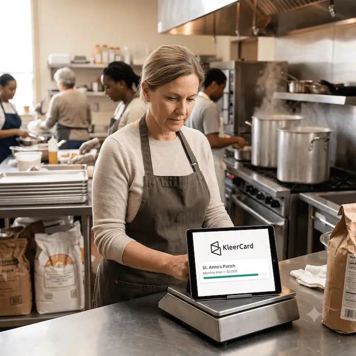 Woman wearing apron using tablet showing KleerCard parish monthly spending limit in a commercial kitchen.