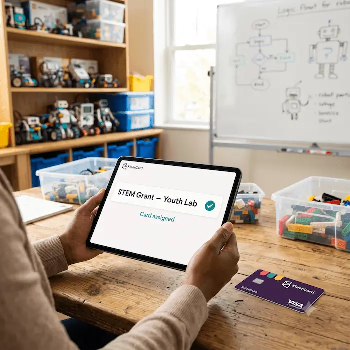 Person holding tablet displaying 'STEM Grant—Youth Lab Card assigned' in a robotics workshop.
