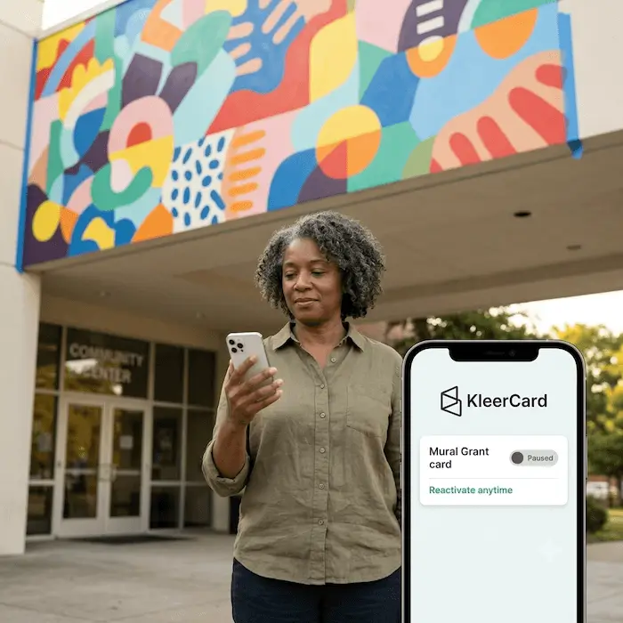 Woman standing outside a community center using a phone app showing a paused KleerCard grant card.