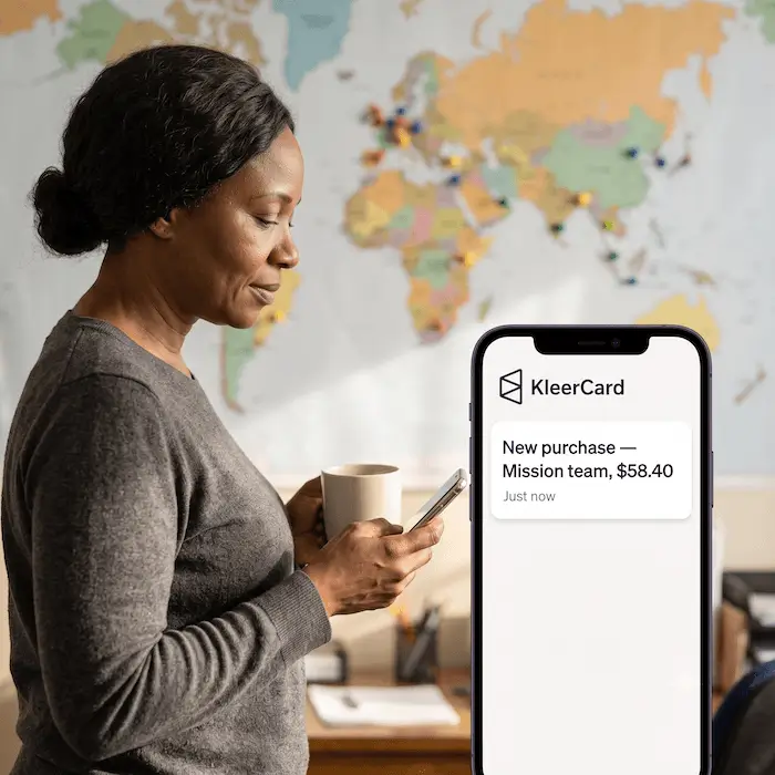 Woman checks phone with KleerCard alert showing $58.40 purchase by Mission team, world map behind her.