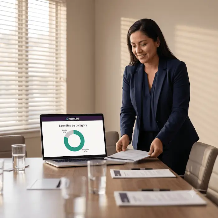 Businesswoman standing by a table with a laptop showing spending by category pie chart.