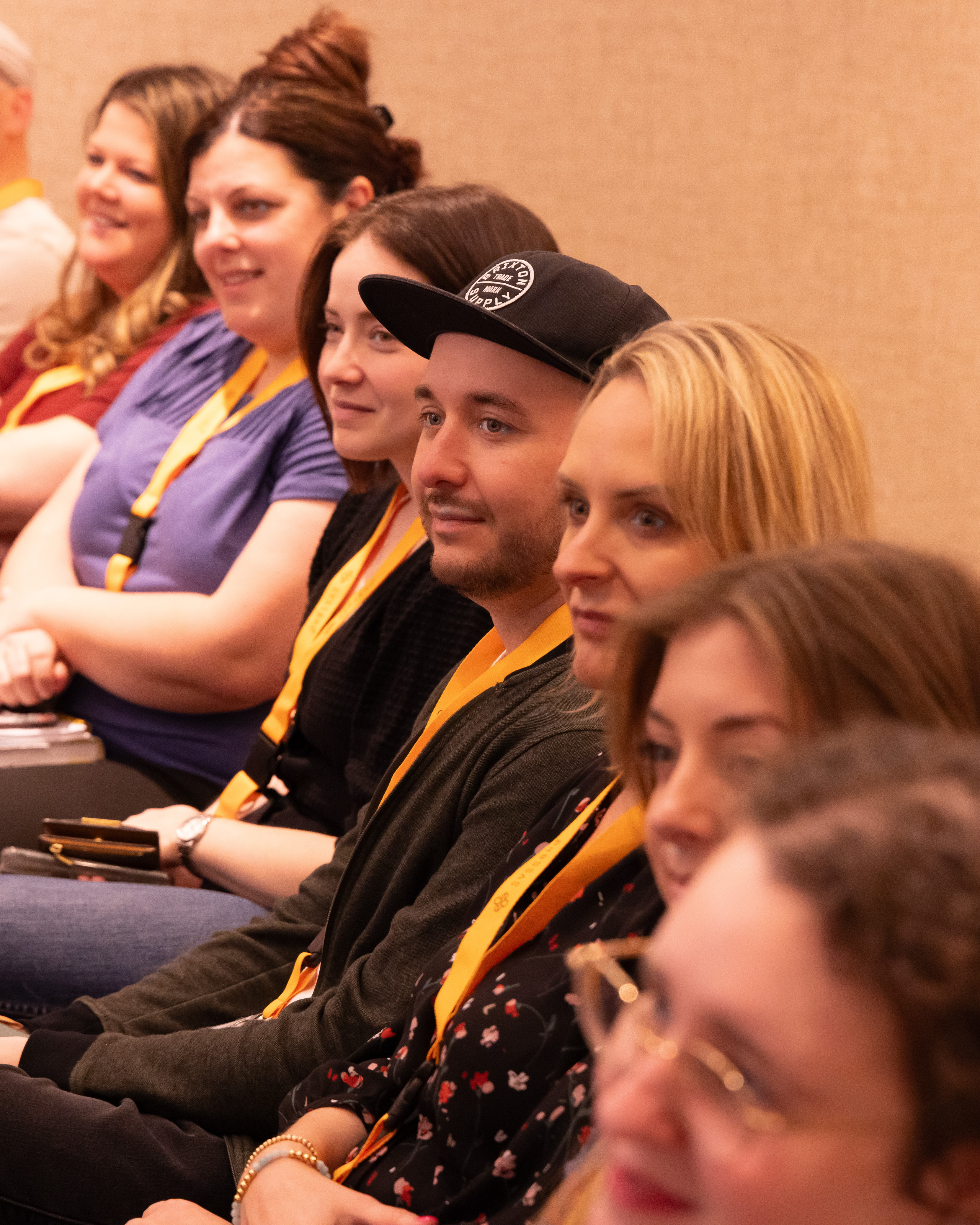Side view of attentive people seated indoors wearing yellow lanyards at an event or conference.