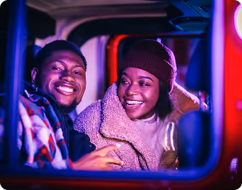 Couple in winter hats smiling out of their car window at the lights