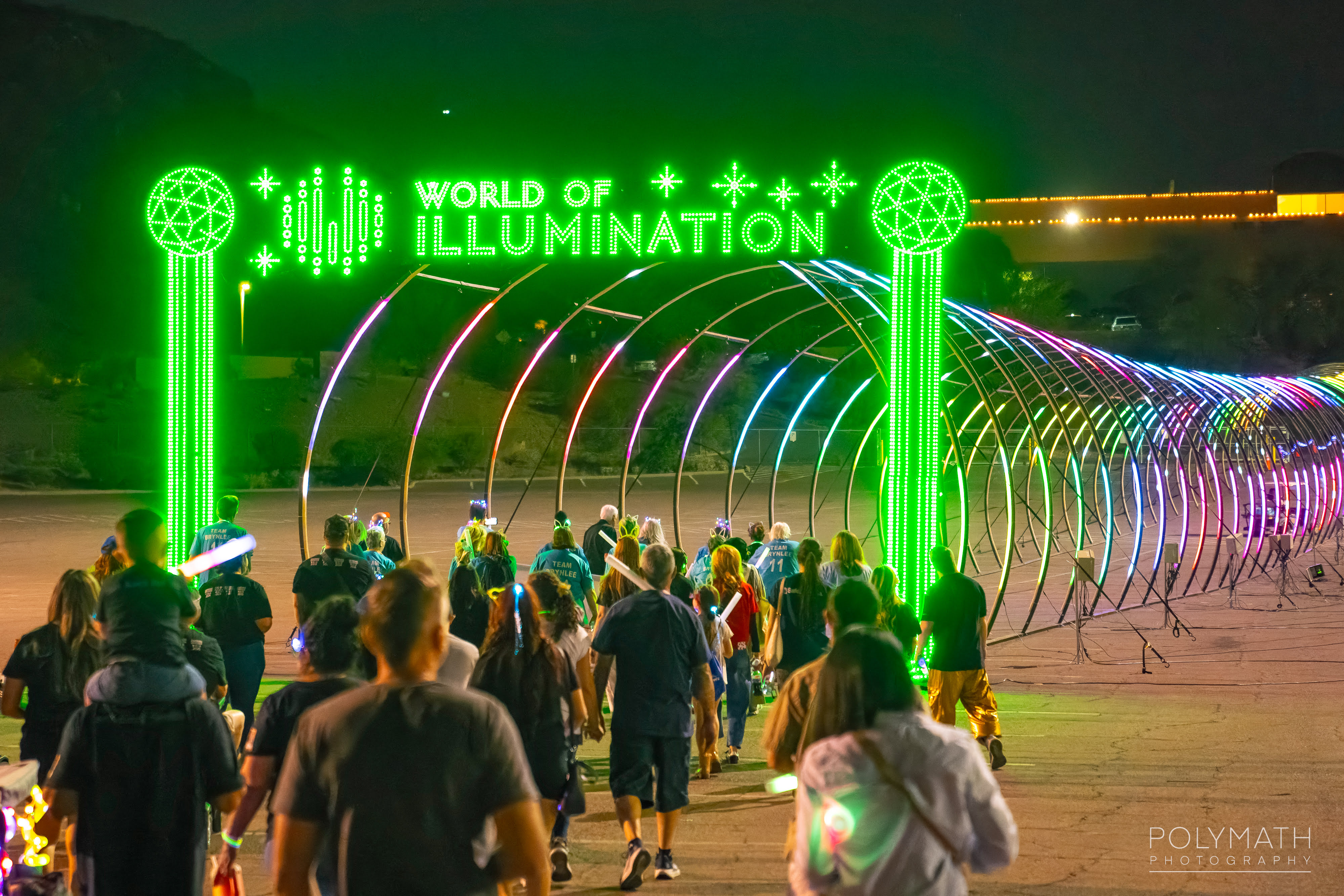 Guests walking under the illuminated World of Illumination arch at a charity walk