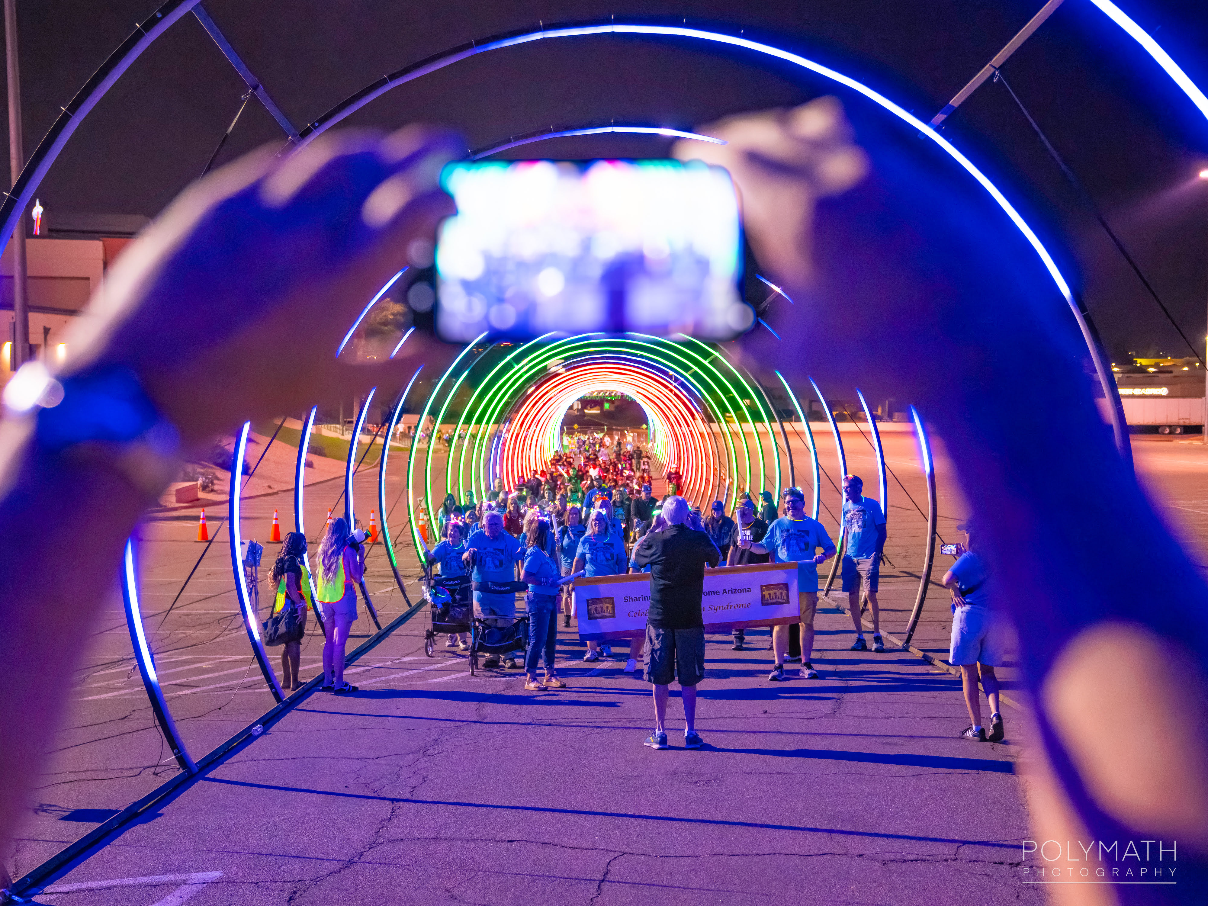 Participants filming on a phone as they walk through a glowing light tunnel
