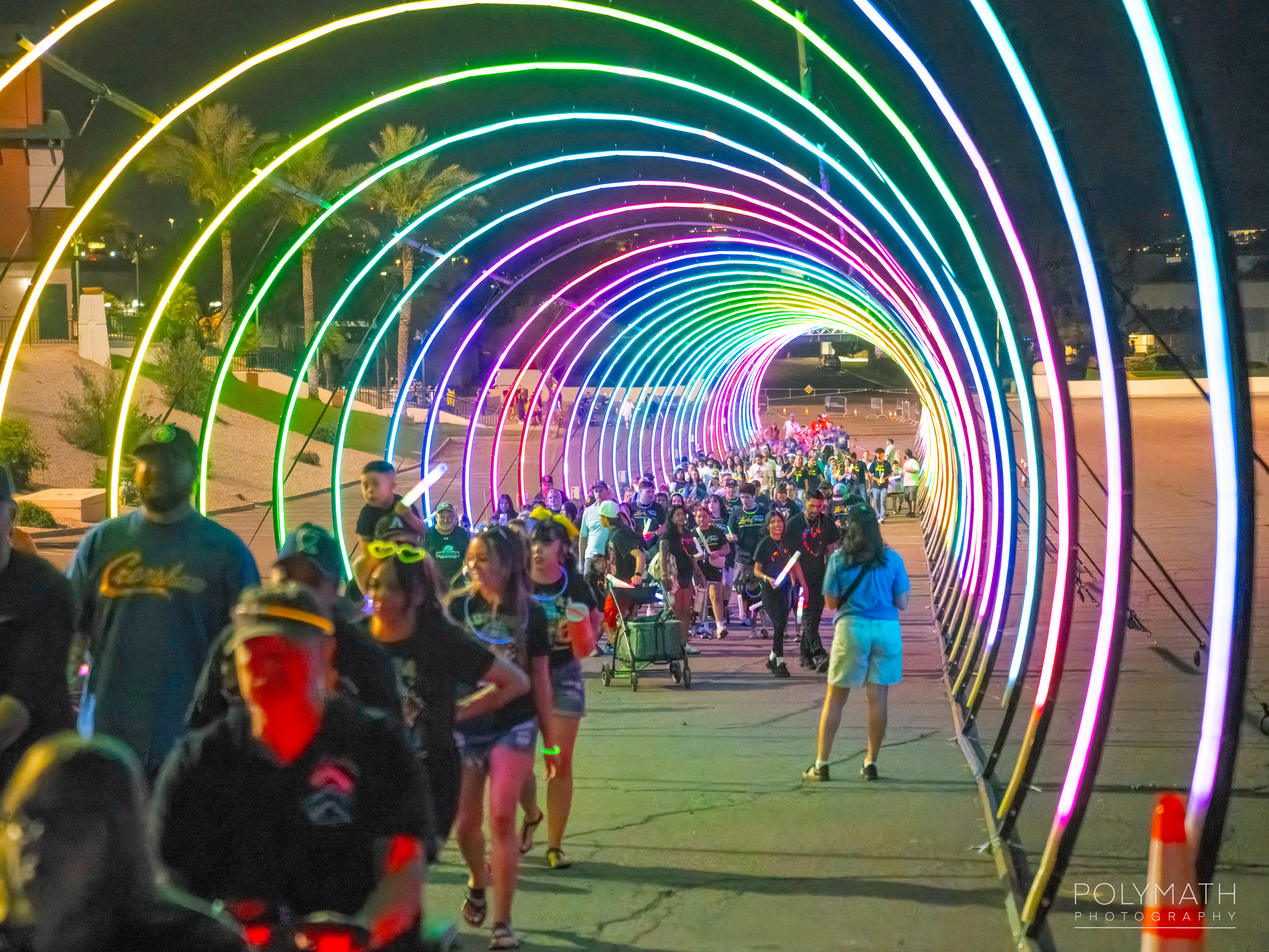Crowd walking through a rainbow light tunnel at a charity walk