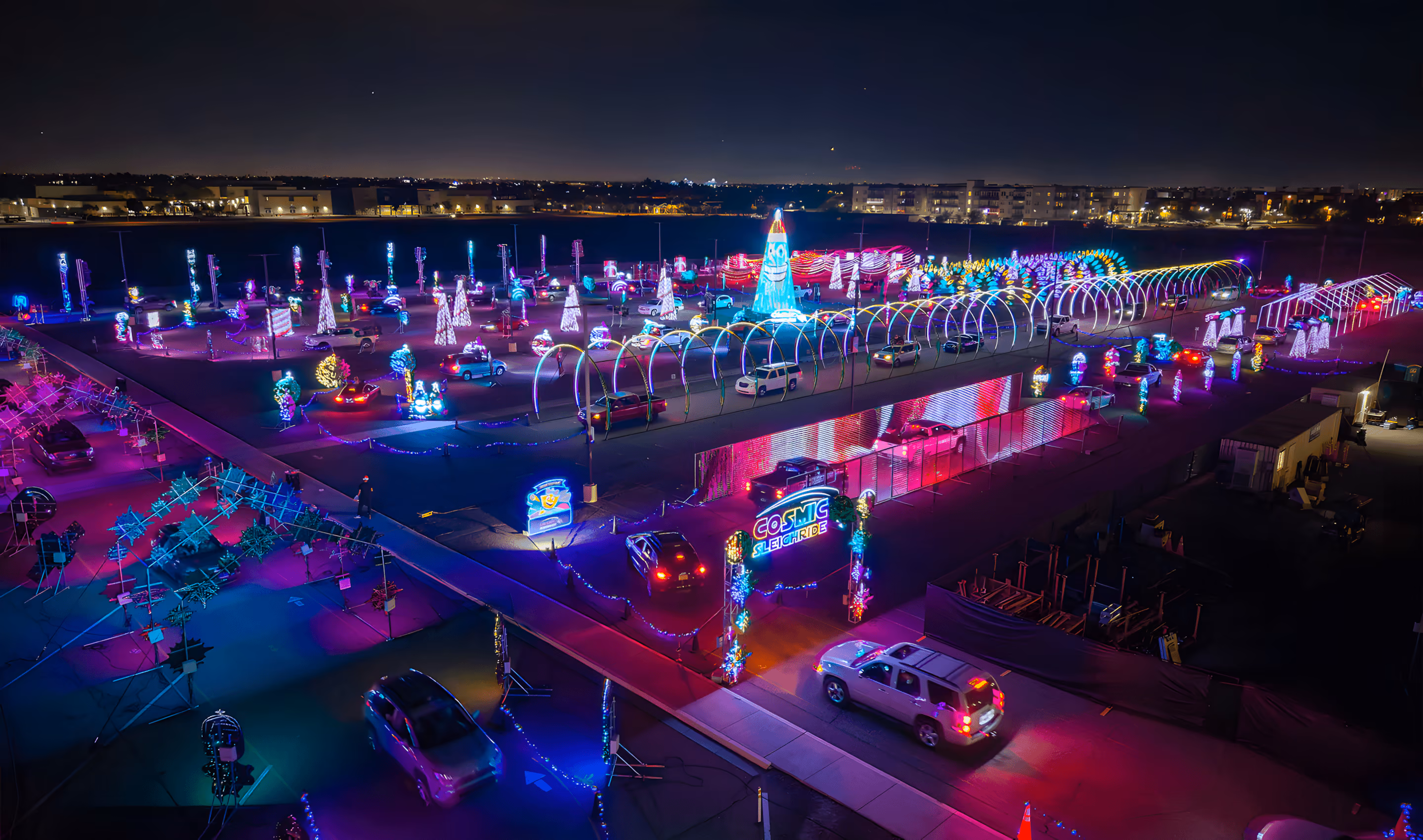 Night aerial view of cars driving through a colorful light display at Cosmic Sleigh Ride event.