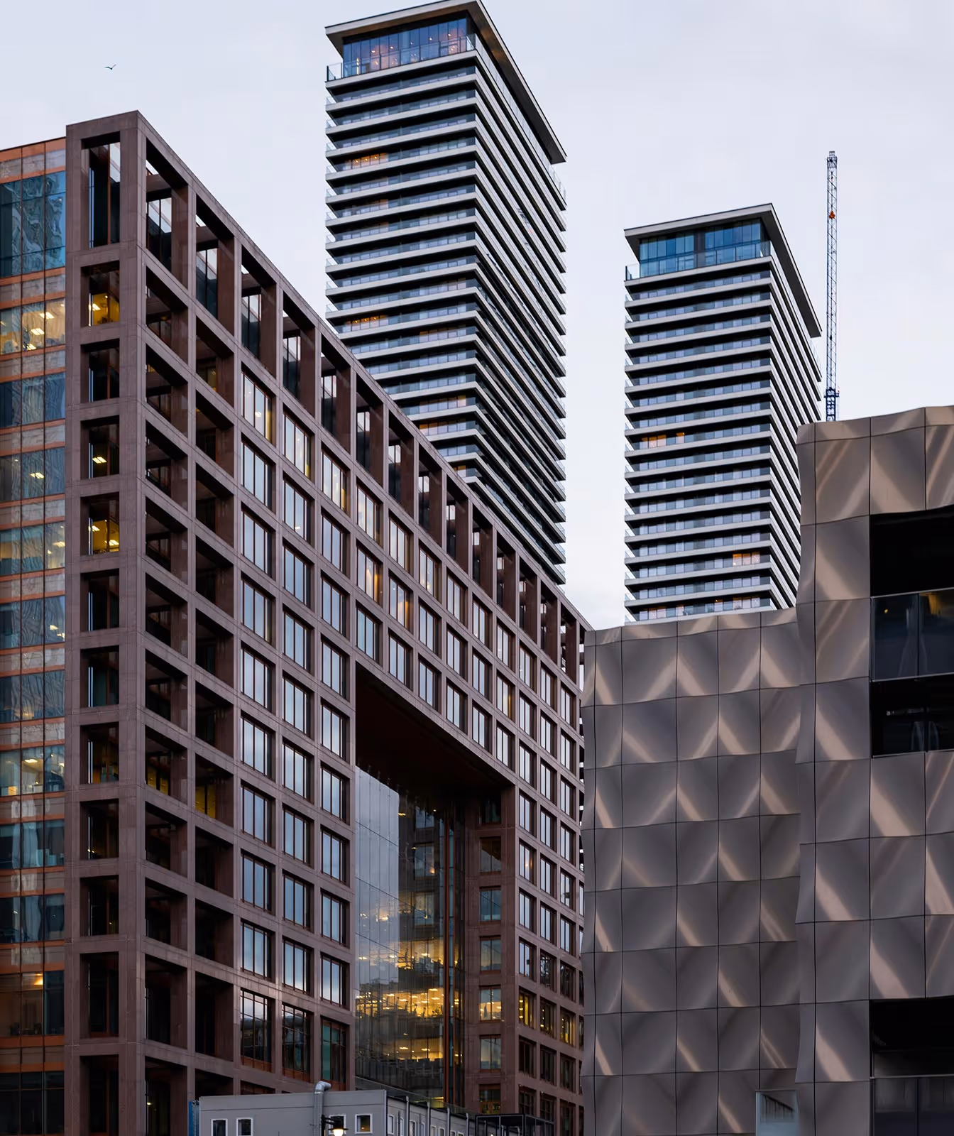 Modern high-rise towers with glass windows and geometric facades against a cloudy sky.