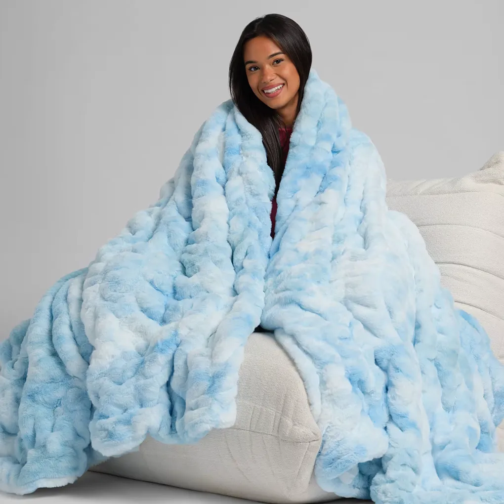 Smiling woman wrapped in a light blue Dreamer Blanket on a couch