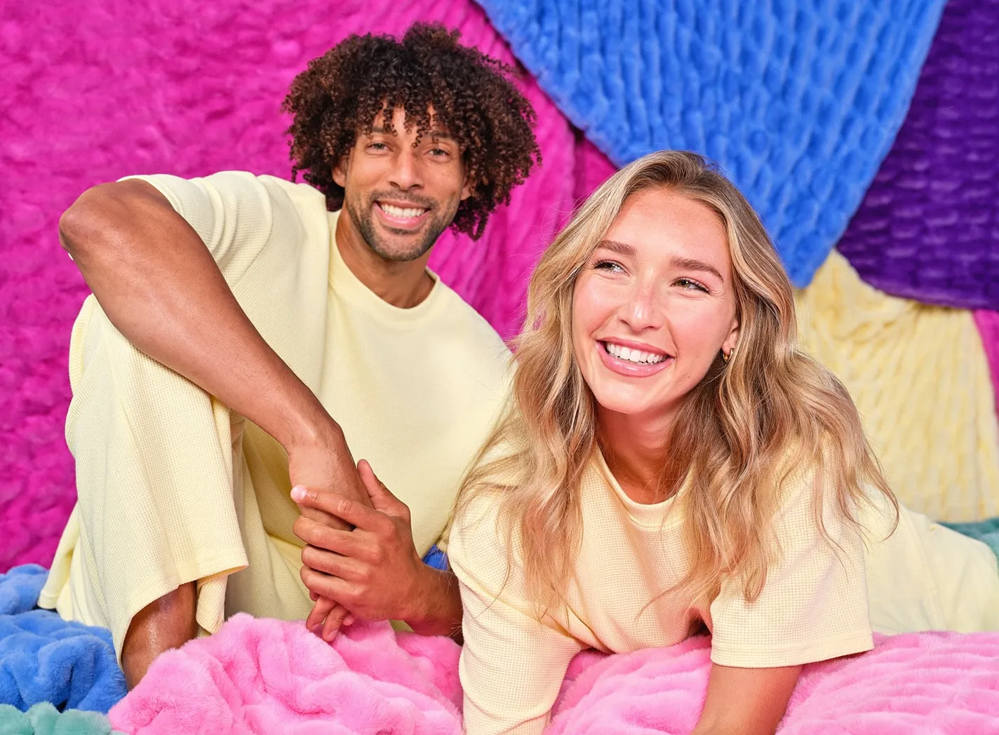 Two people lying on a pile of colorful Dreamer Blankets. 30 days money back guarantee.