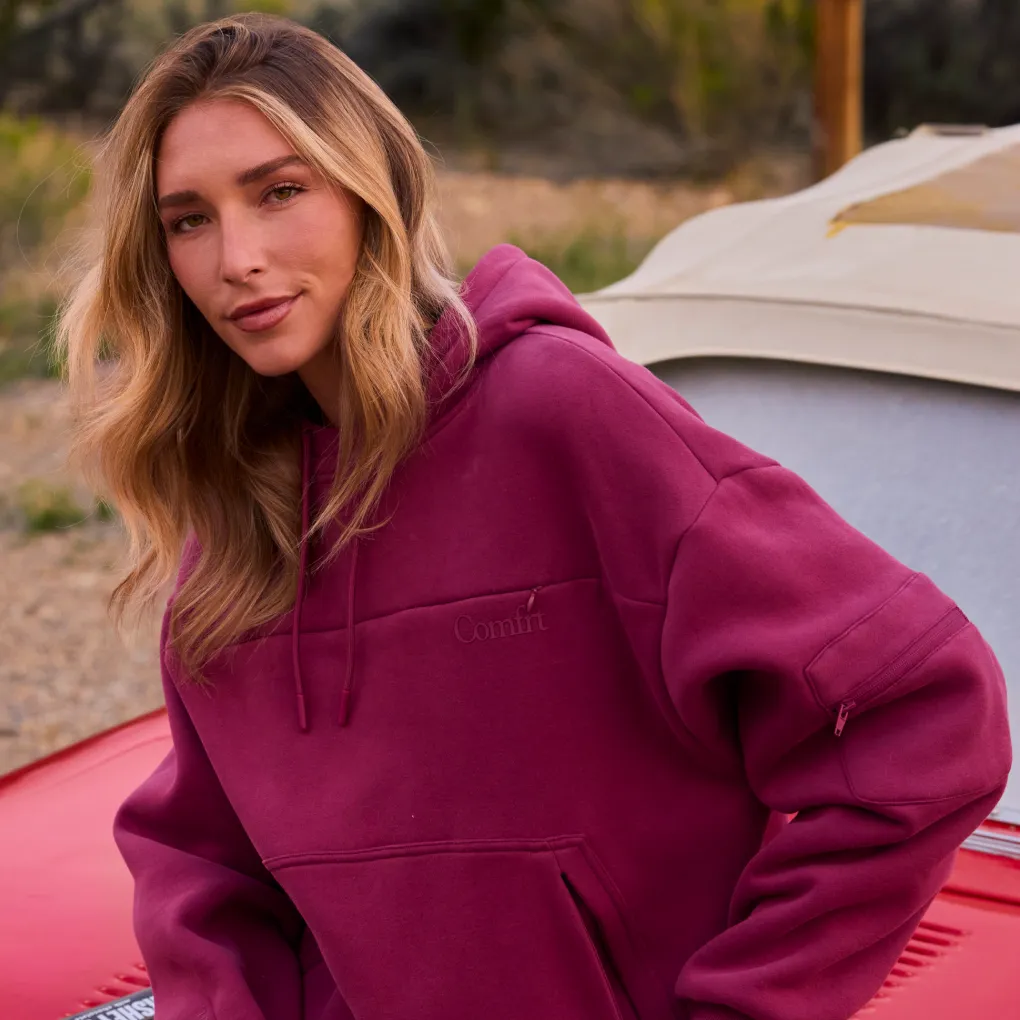 Woman outdoors at a campsite wearing an oversized berry-red Snak Hoodie in heavyweight CloudTouch fleece