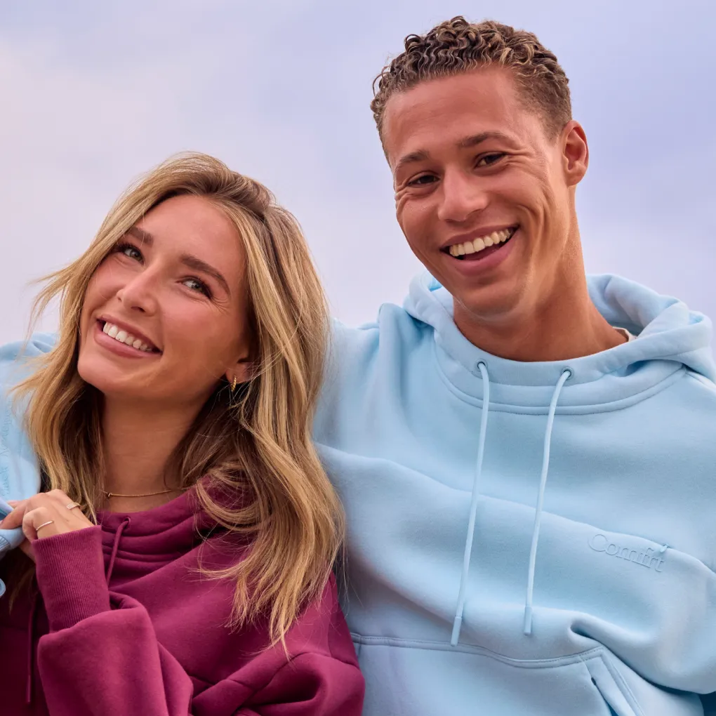 Smiling couple wearing Comfrt Snak Hoodies in berry red and light blue