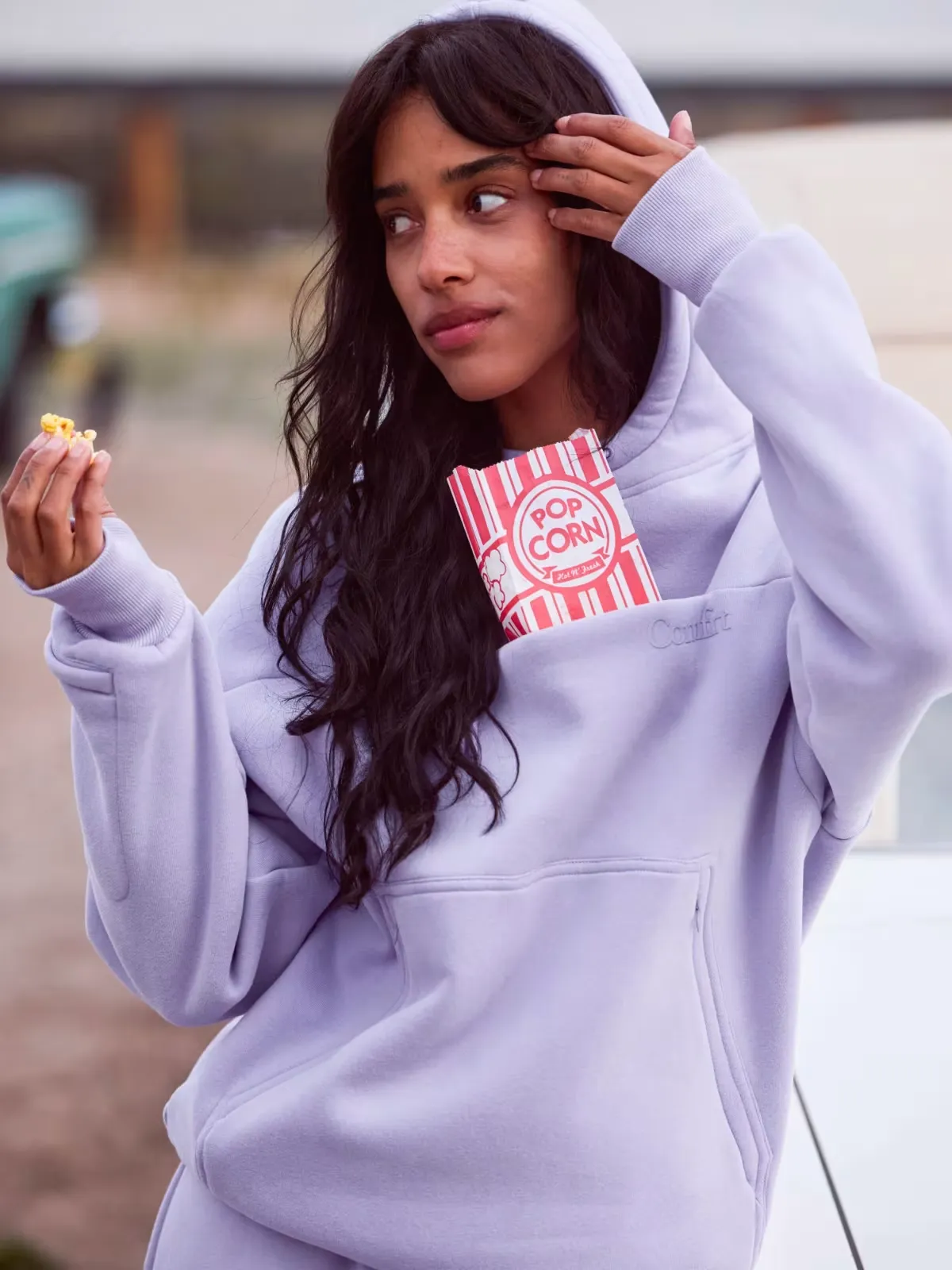 Woman in a brown Snak Hoodie placing a snack into the front pocket