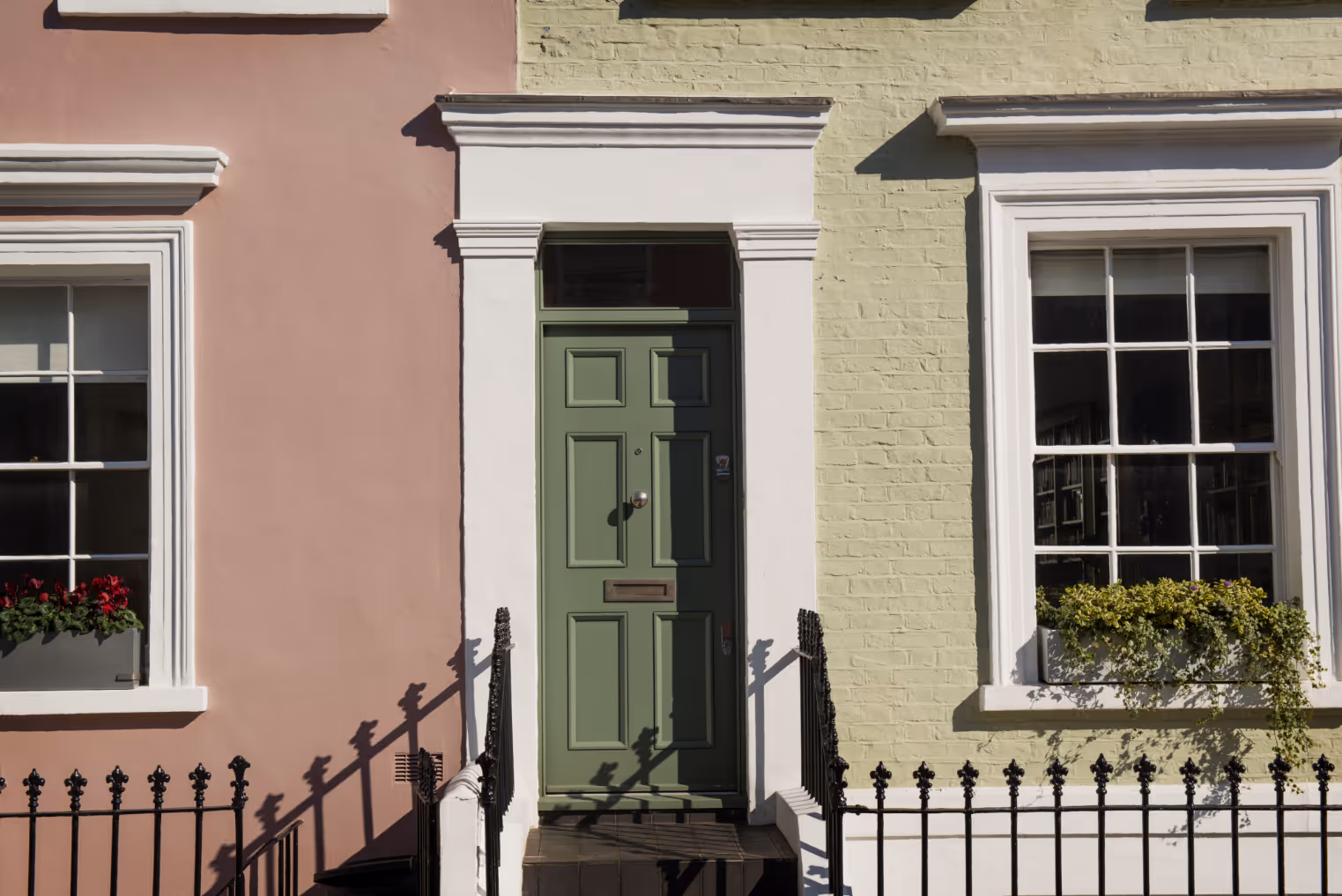 Green front door with white trim between orange-beige and light yellow brick walls with windows and flower boxes.