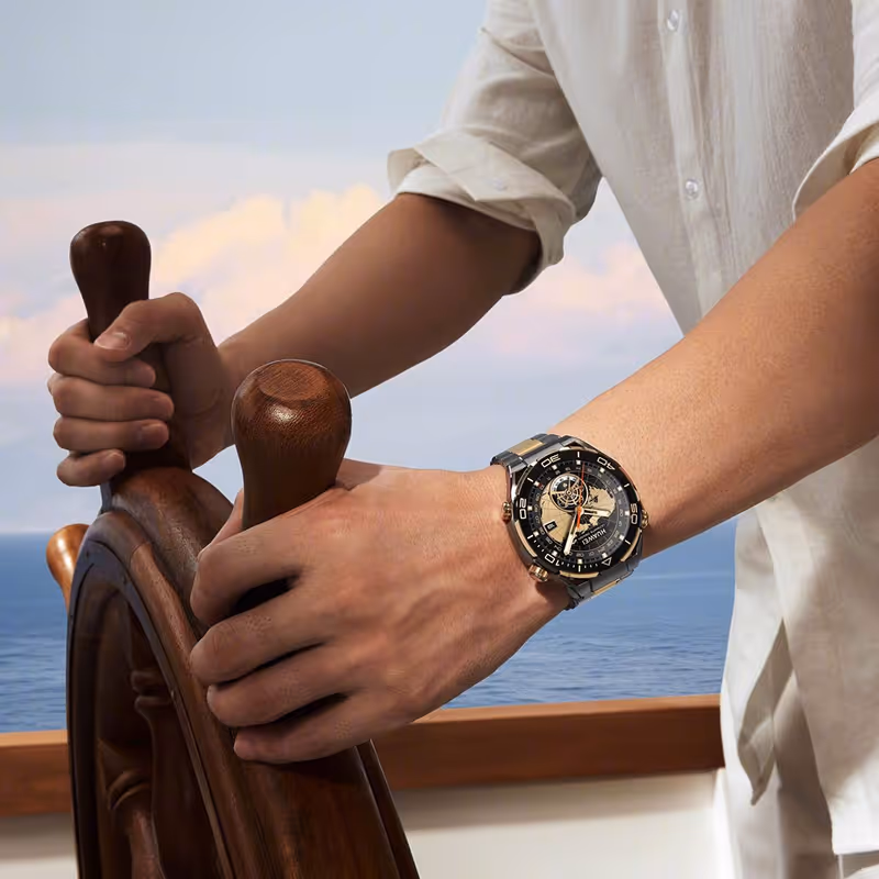 Person steering a wooden ship's wheel wearing a silver and black wristwatch with a map design.