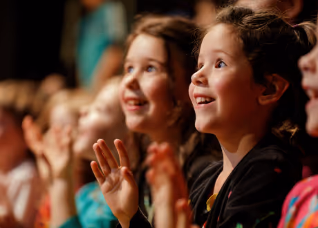 Close-up of smiling children attentively watching and clapping in a warmly lit setting.